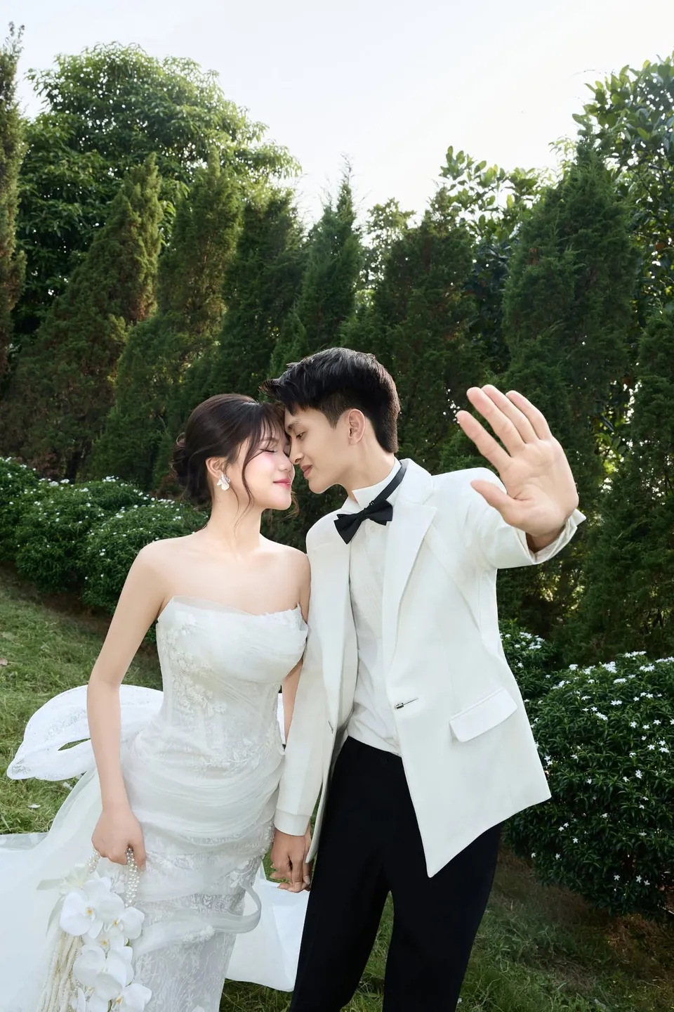 Cô dâu và chú rể vẫy tay cười giữa hàng cây xanh