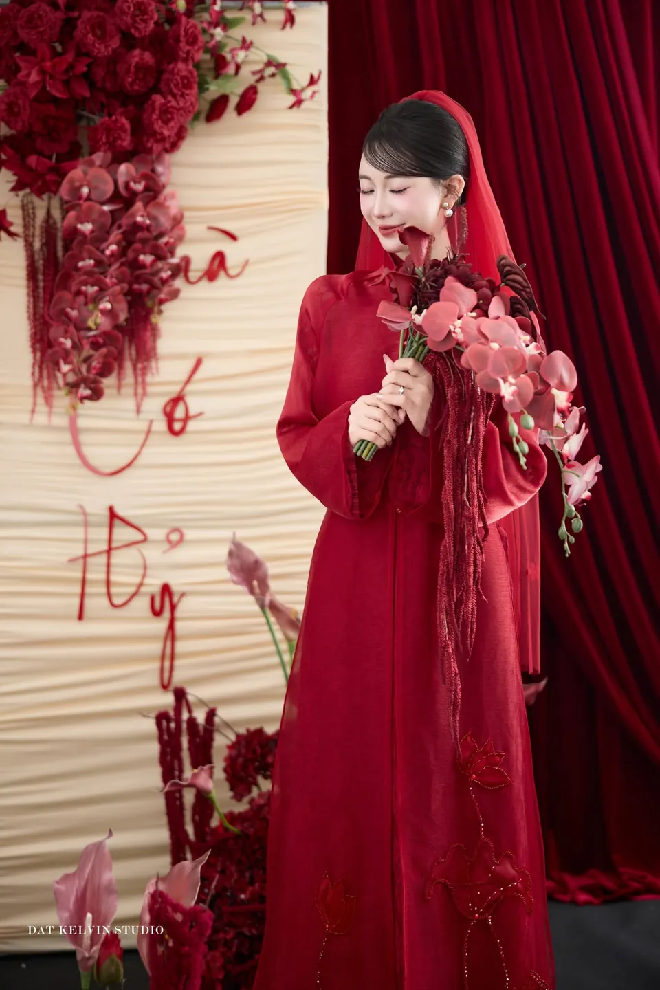 Cô dâu áo dài đỏ, khăn voan đỏ, cầm bó hoa lan