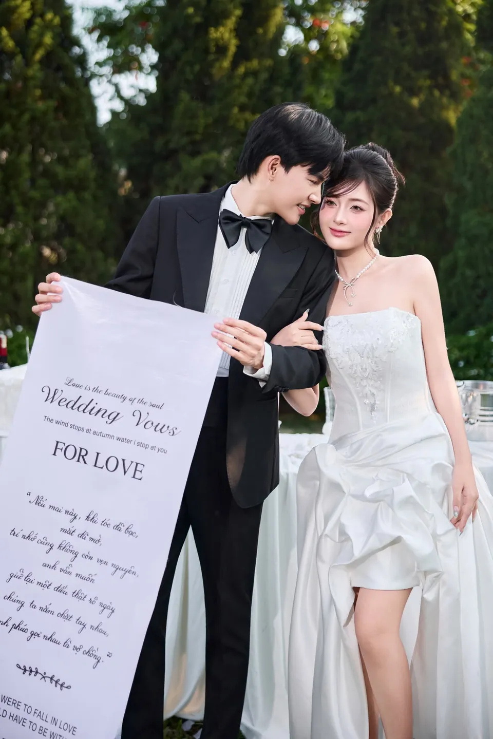 Chú rể tựa đầu vào cô dâu, cùng cầm bản lời thề Wedding Vows