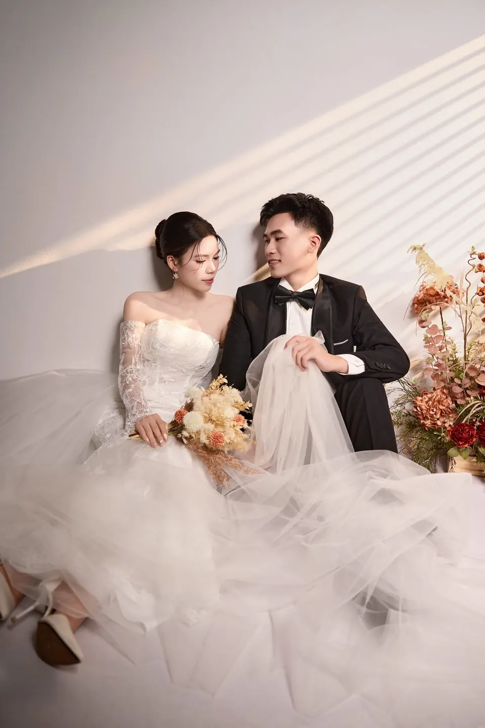 Cô dâu và chú rể ngồi tựa vào nhau bên bình hoa khô