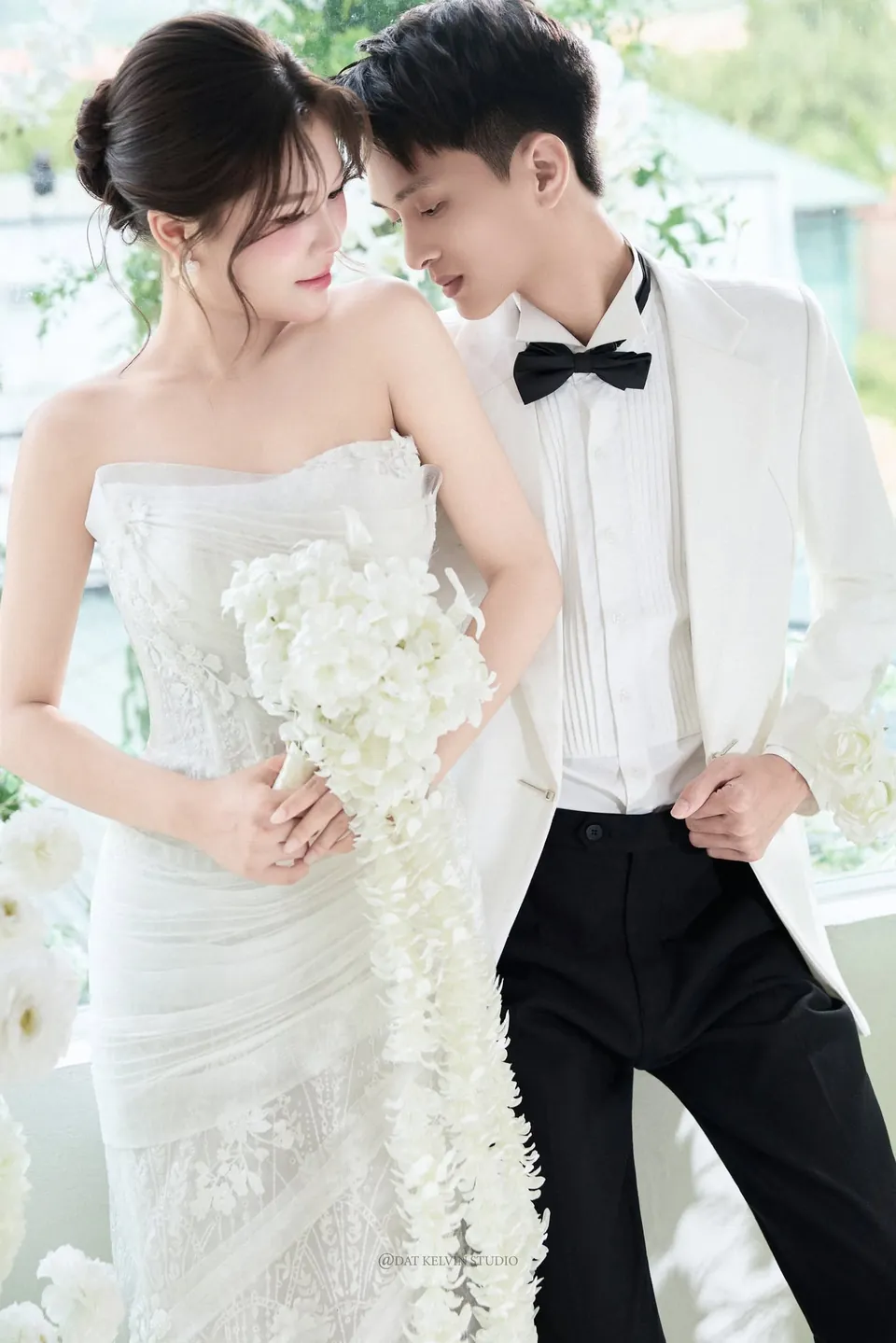 Cô dâu cầm thác hoa trắng tựa vào chú rể