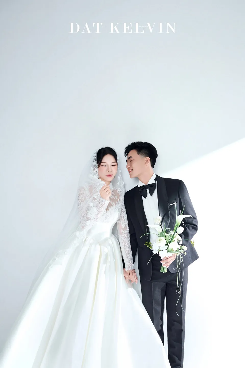 Chú rể cầm hoa loa kèn đứng cạnh cô dâu khăn voan dài