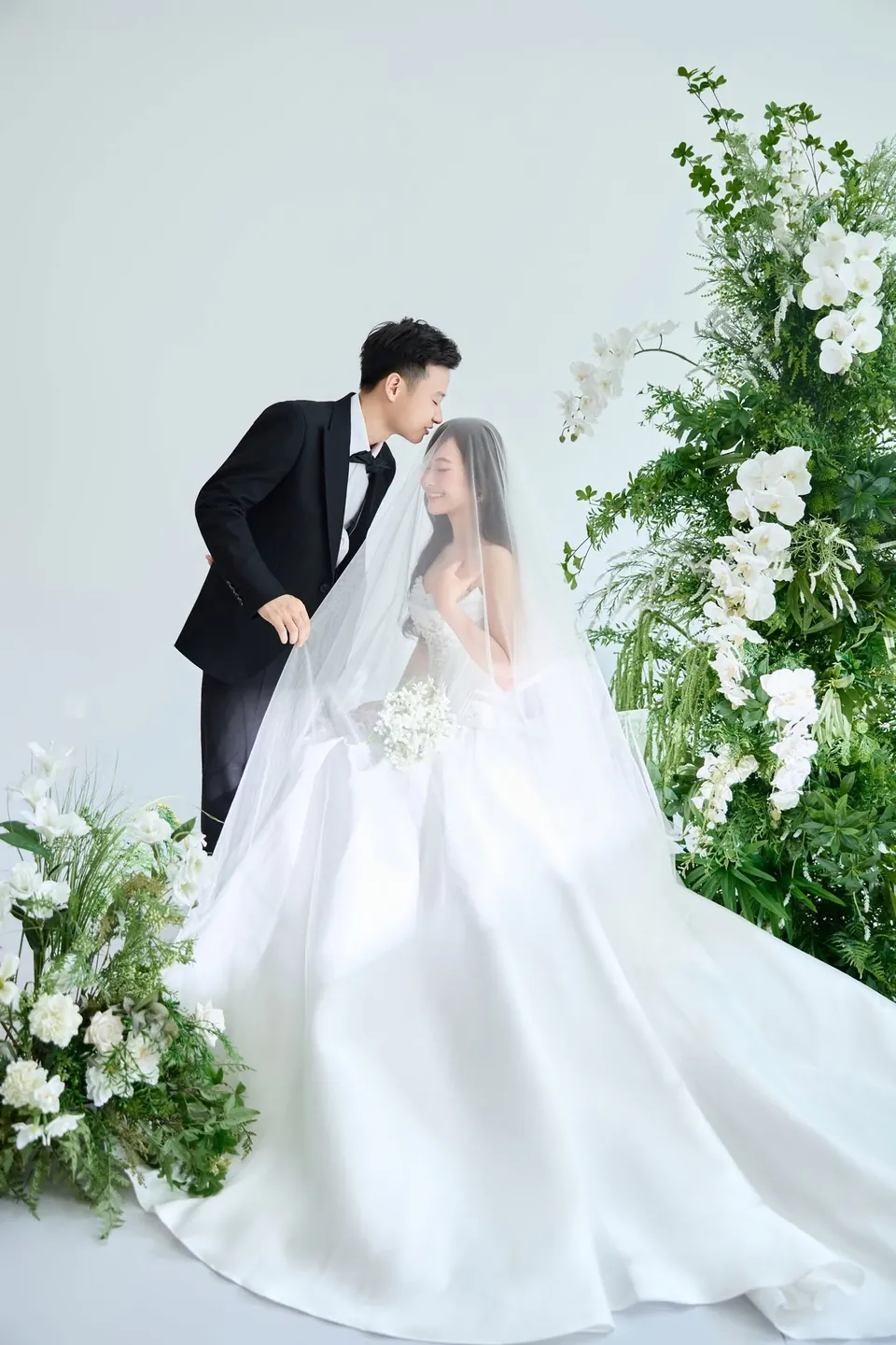 Chú rể hôn cô dâu ngồi trên tà váy xòe giữa hoa lá
