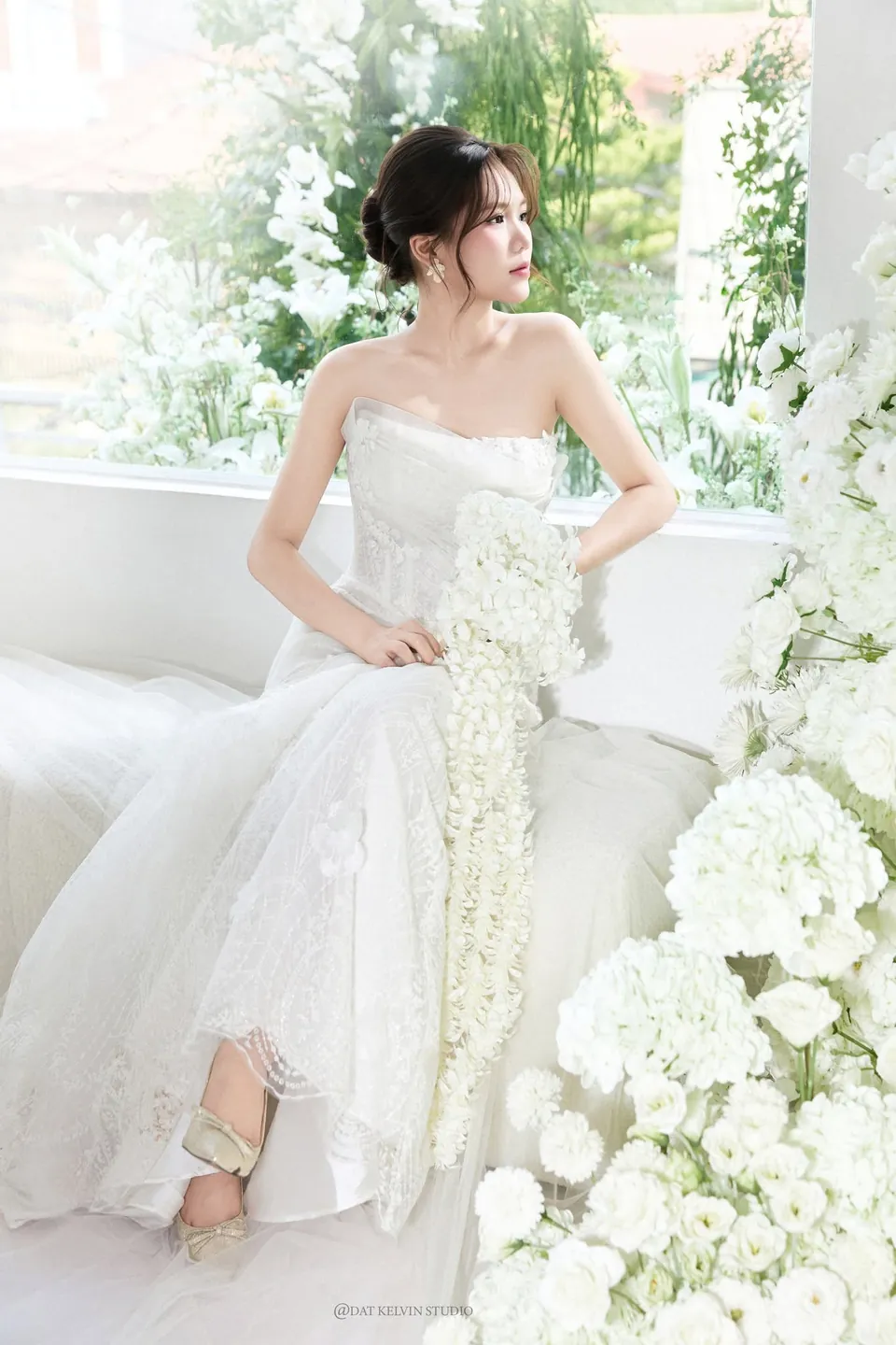 Cô dâu váy đuôi cá ngồi bên khung cửa trang trí hoa trắng