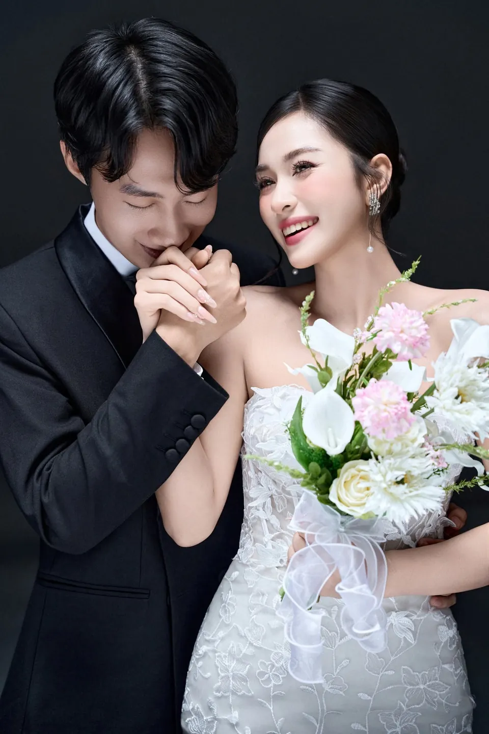 Chú rể hôn tay cô dâu cầm bó hoa trắng hồng