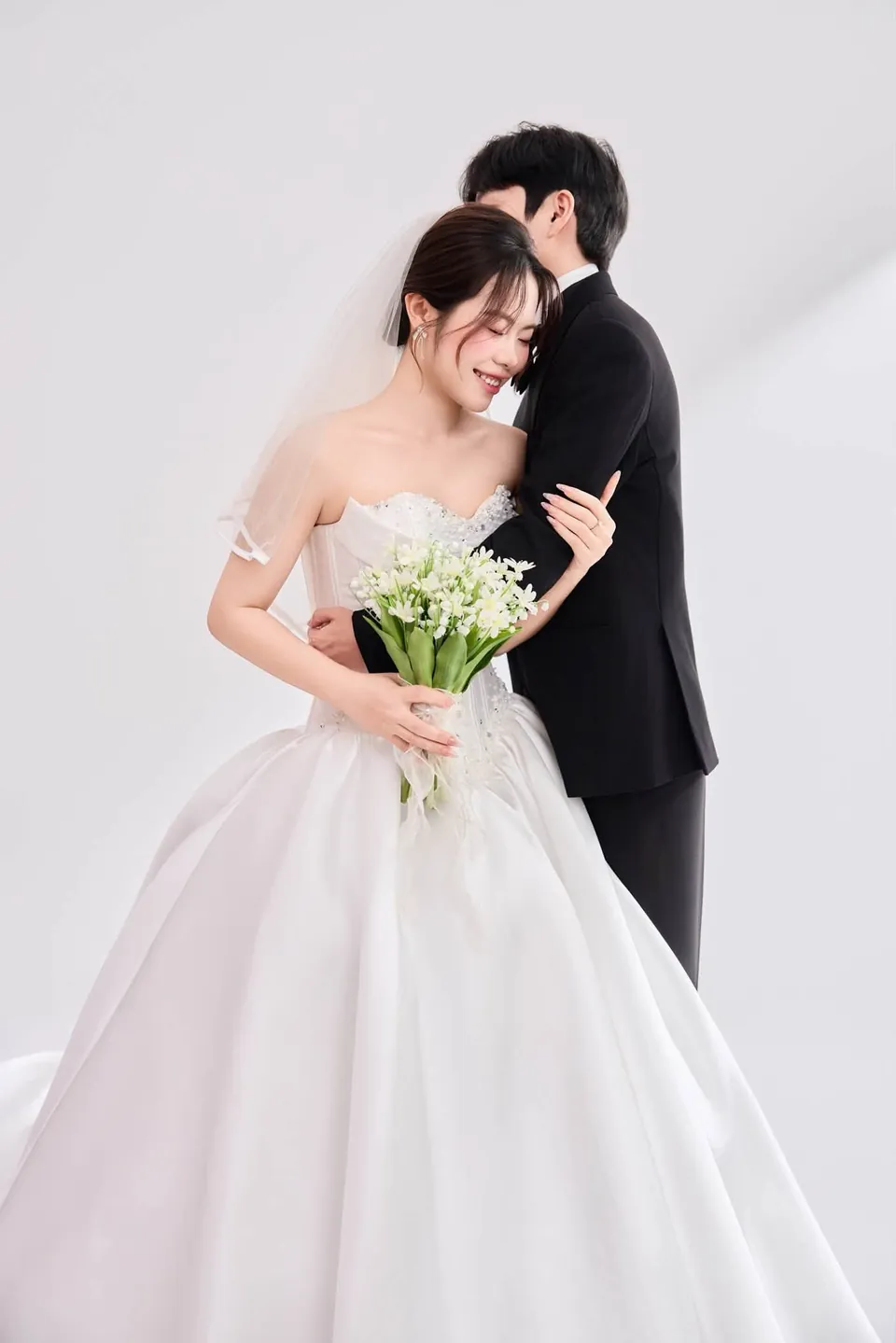 Chú rể ôm cô dâu cầm bó hoa linh lan