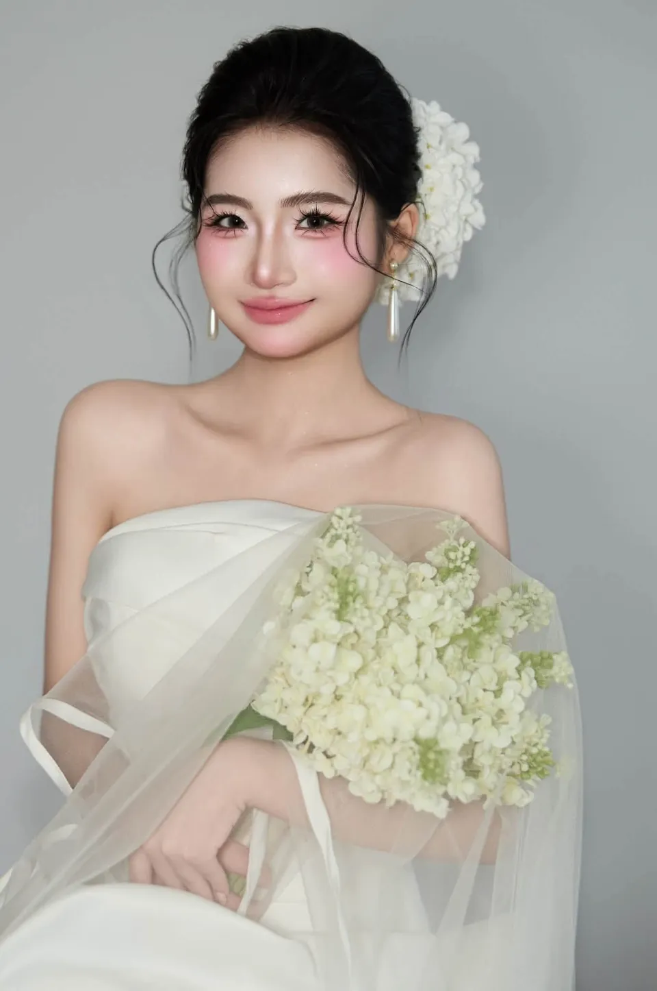 Cô dâu trang điểm má hồng ôm bó hoa trắng