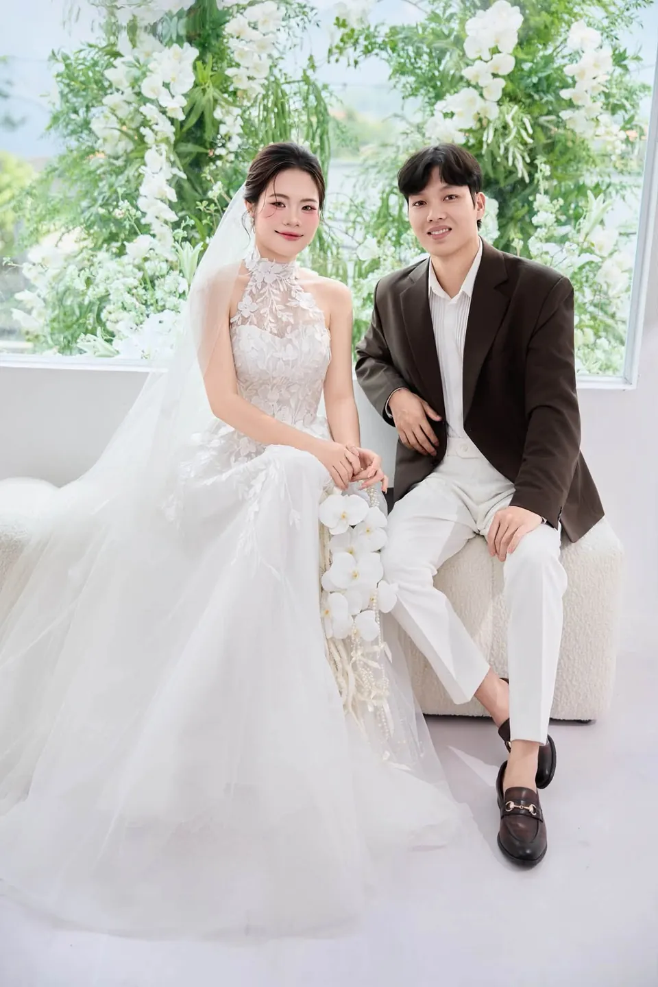 Cặp đôi ngồi cạnh nhau, cô dâu mặc váy cưới với khăn voan dài