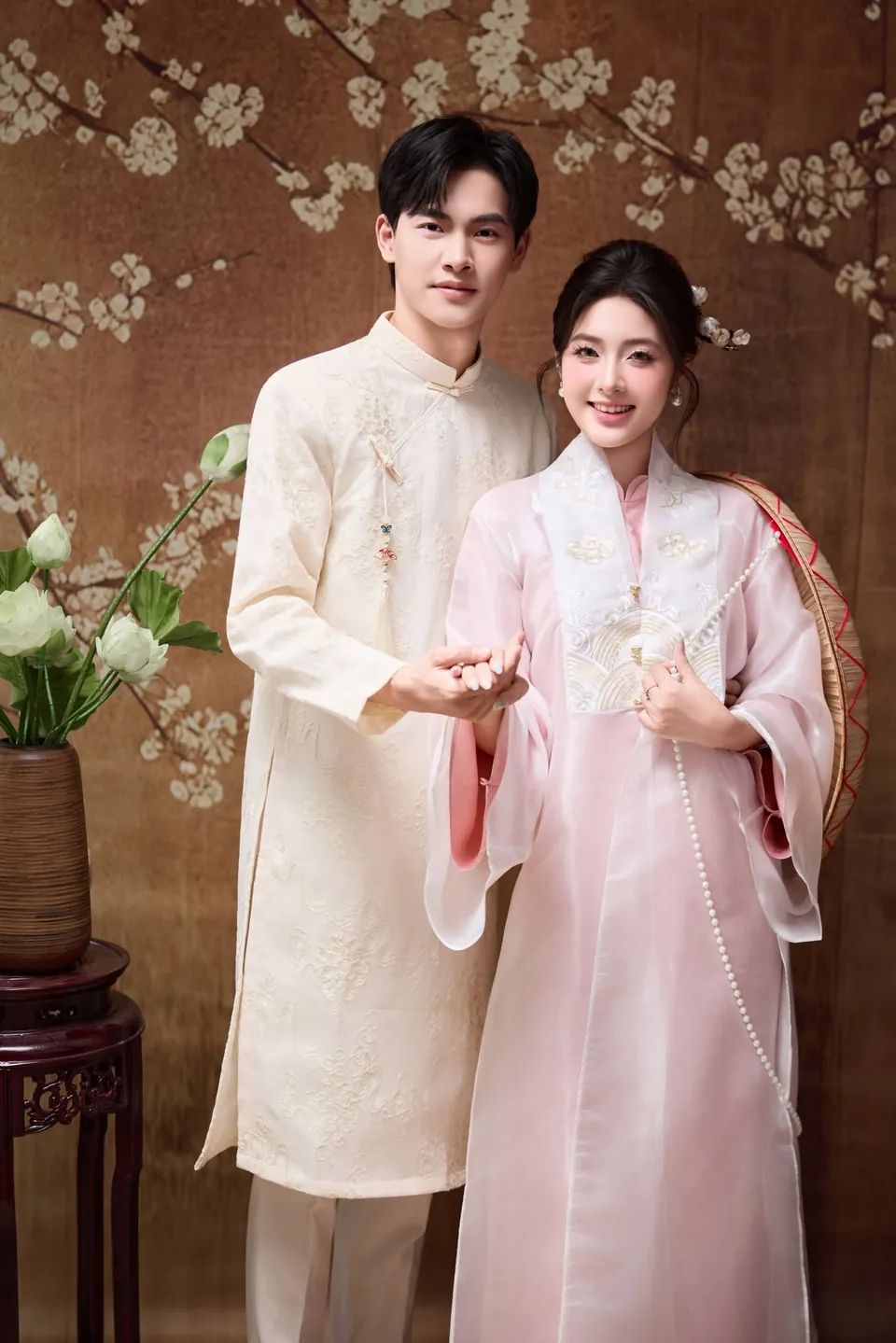 Chú rể áo dài trắng nắm tay cô dâu áo dài hồng, cả hai mỉm cười