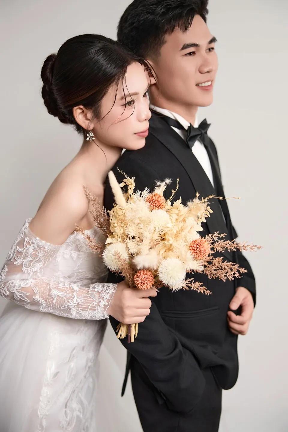 Cô dâu cầm bó hoa khô tựa vào vai chú rể vest đen