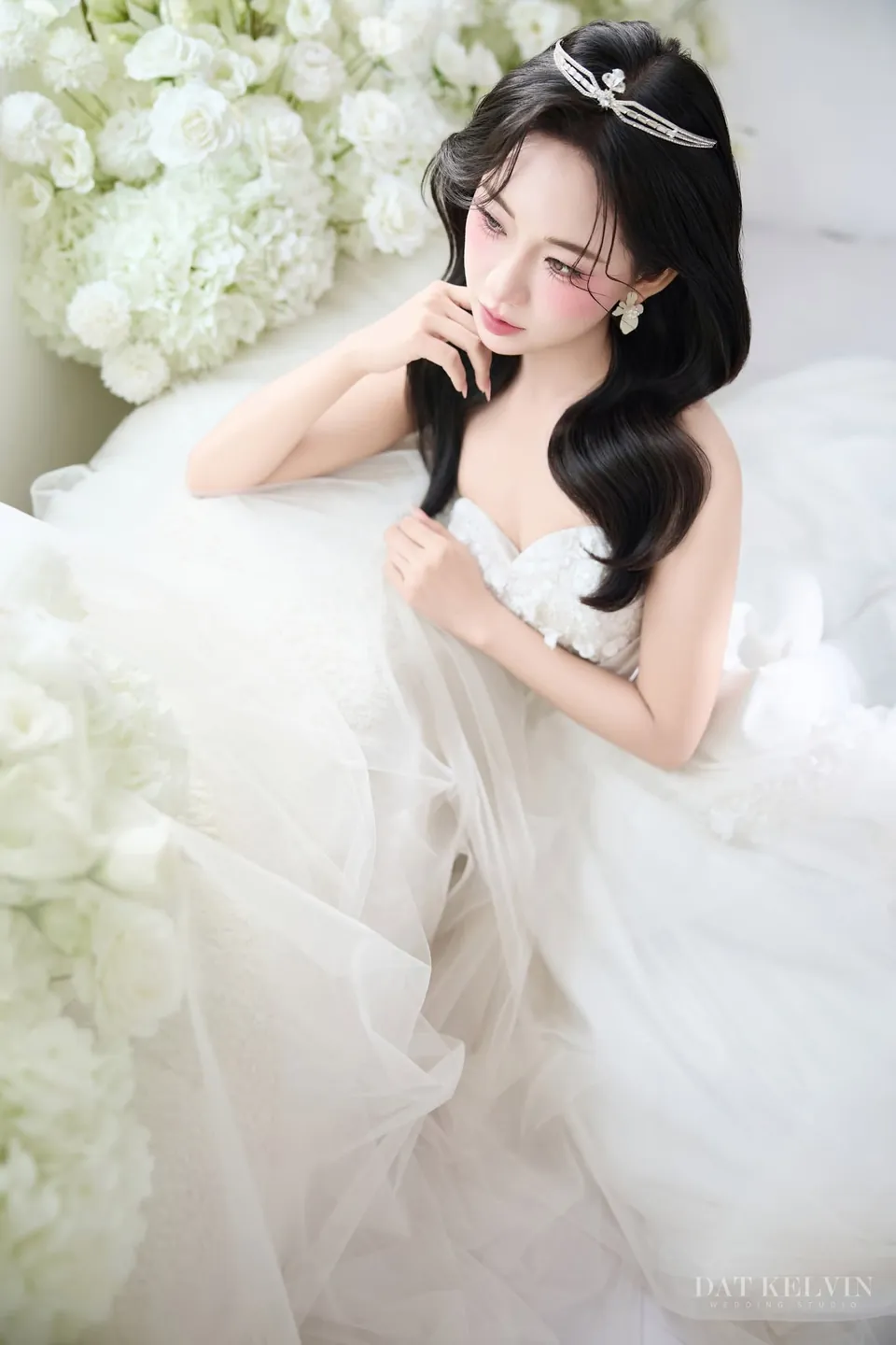 Cô dâu đội vương miện ngồi giữa tà váy trắng và hoa