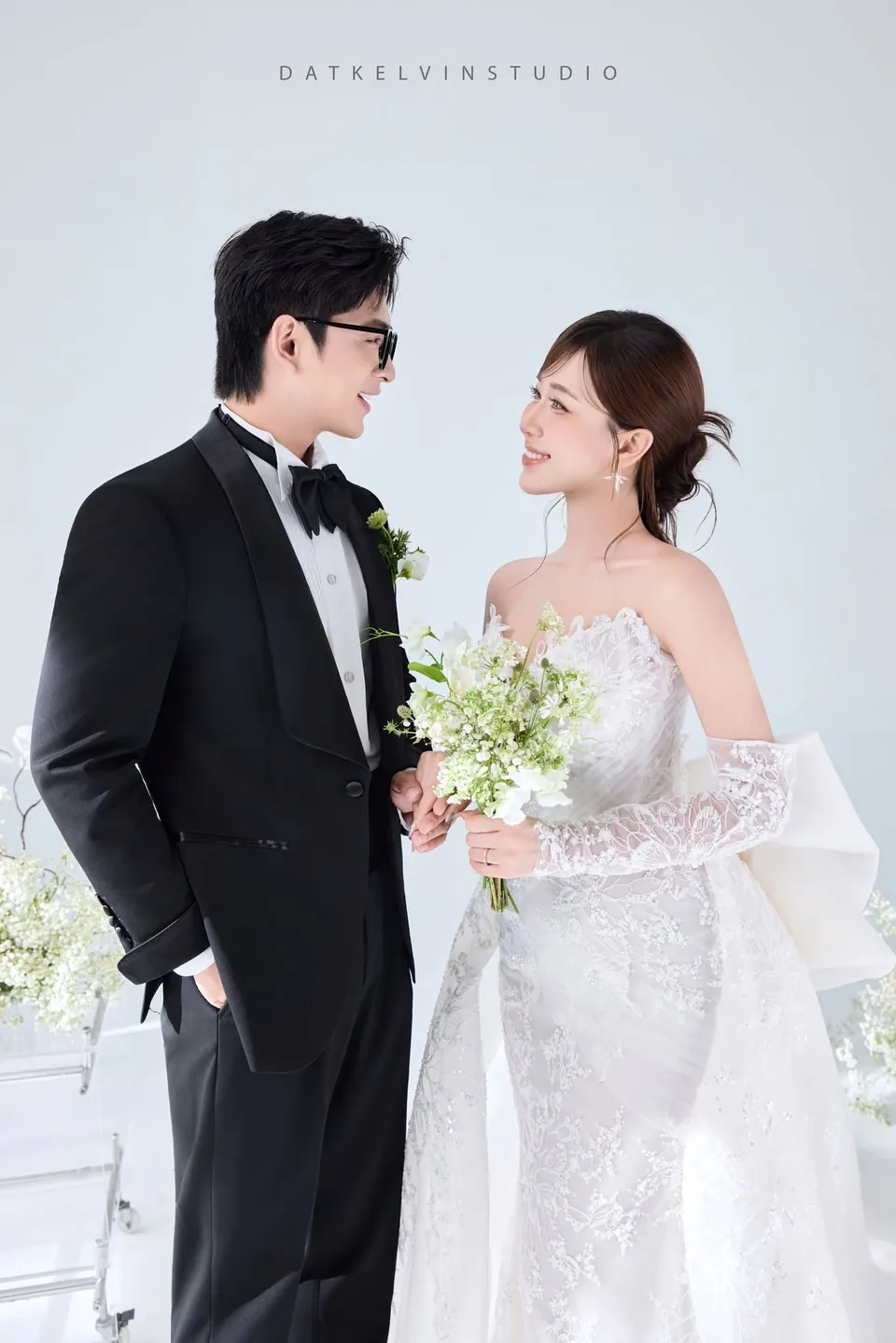 Cô dâu cầm bó hoa xanh trắng mỉm cười nhìn chú rể